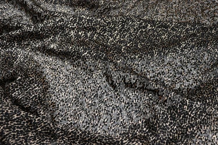 a close-up view of a fabric with a distinctive leopard print pattern. The fabric appears to be a blend of black and gray colors, creating a visually striking and textured appearance.