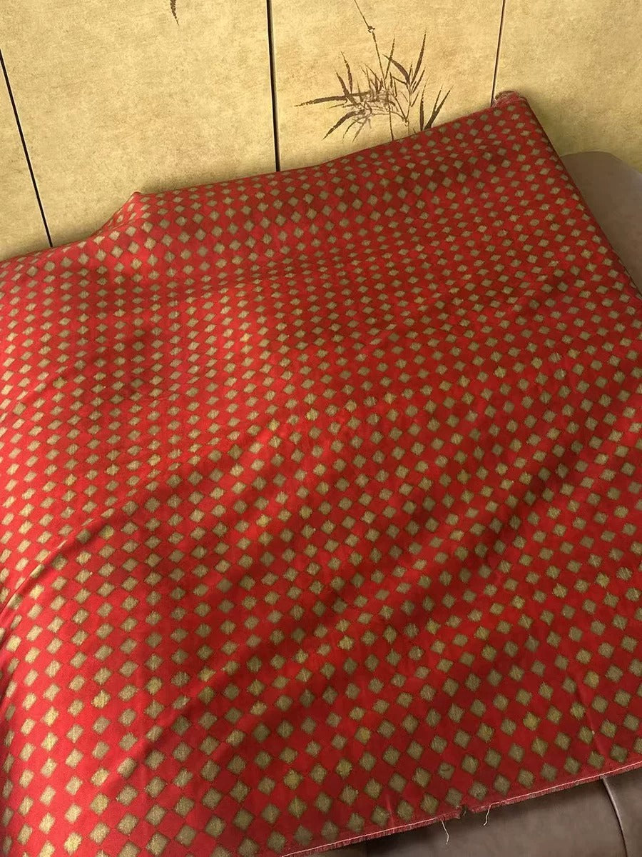 a red and gold patterned fabric, possibly a blanket or cushion, placed on a surface.