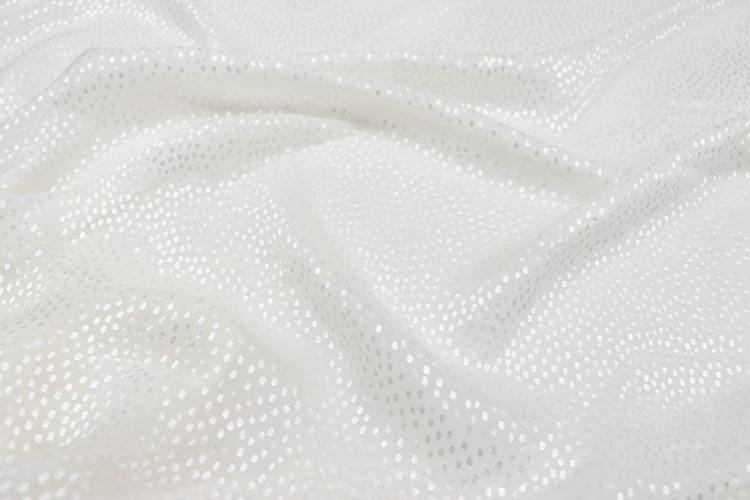 a close-up view of a white fabric with small white dots or sequins, creating a textured and shiny appearance.