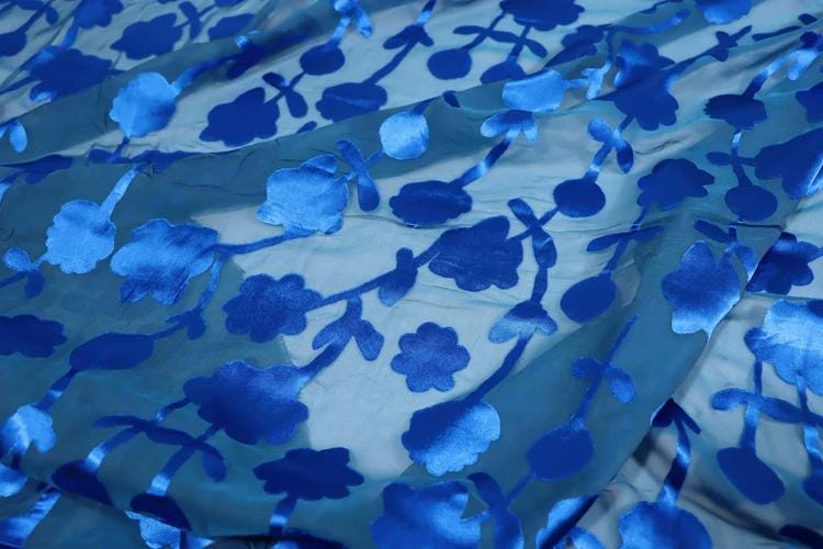 a close-up view of a fabric with a blue floral pattern. The fabric appears to be made of a sheer material, with the blue flowers and leaves creating a visually striking design.
