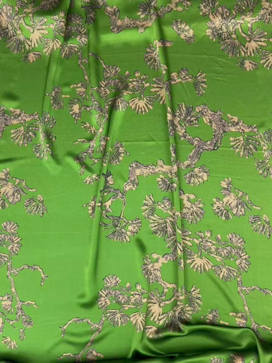 a close-up view of a fabric with a green and beige floral pattern. The fabric appears to be made of silk or a similar material, and the pattern consists of various shades of green and beige flowers and leaves. The fabric is crumpled, giving it a textured appearance.