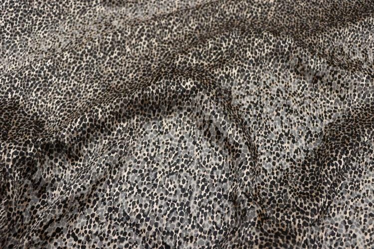 a close-up view of a fabric with a distinctive leopard print pattern. The fabric appears to be made of a material with a textured surface, resembling the appearance of a leopard's fur. The pattern consists of small, irregularly shaped dots or spots in various shades of gray and black, creating a visually striking and intricate design.