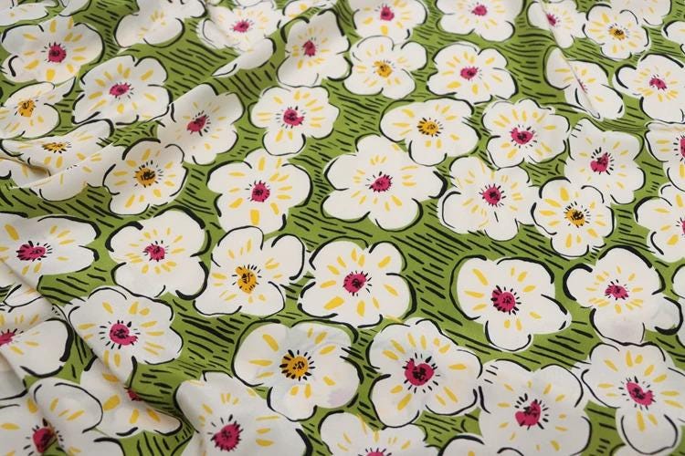 a close-up view of a fabric with a repeating pattern of white flowers with yellow centers against a green background.