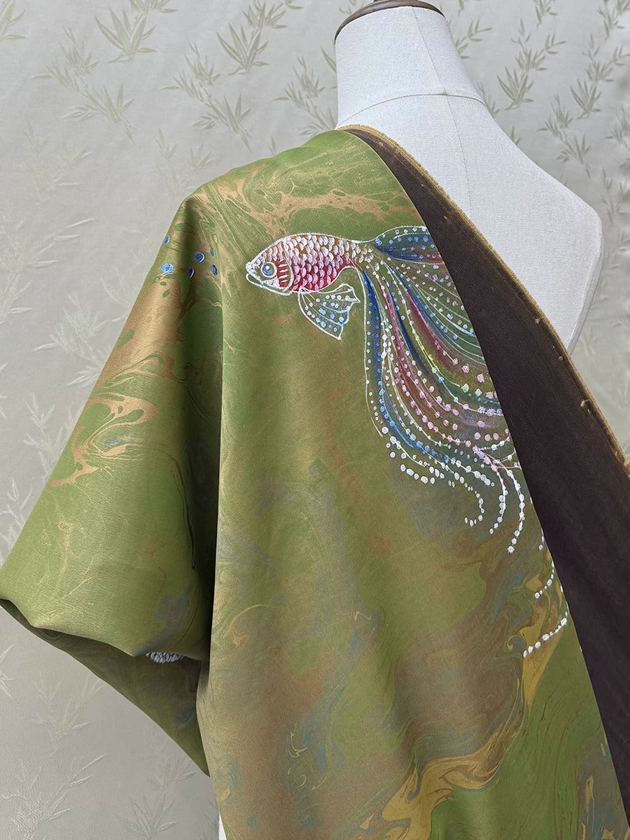 A mannequin wearing a green and gold kimono with a fish design on the sleeve.