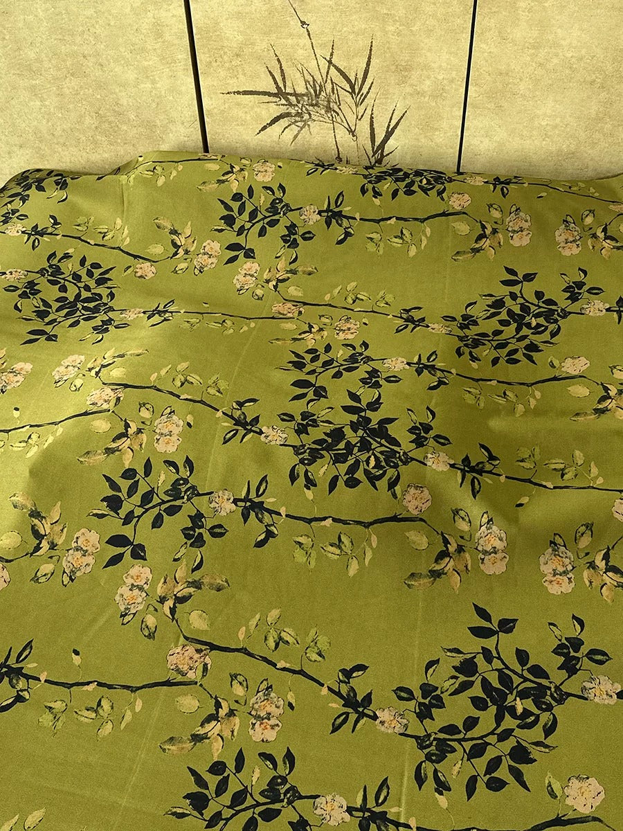 a green fabric with a floral pattern, featuring leaves and flowers in shades of green and black.