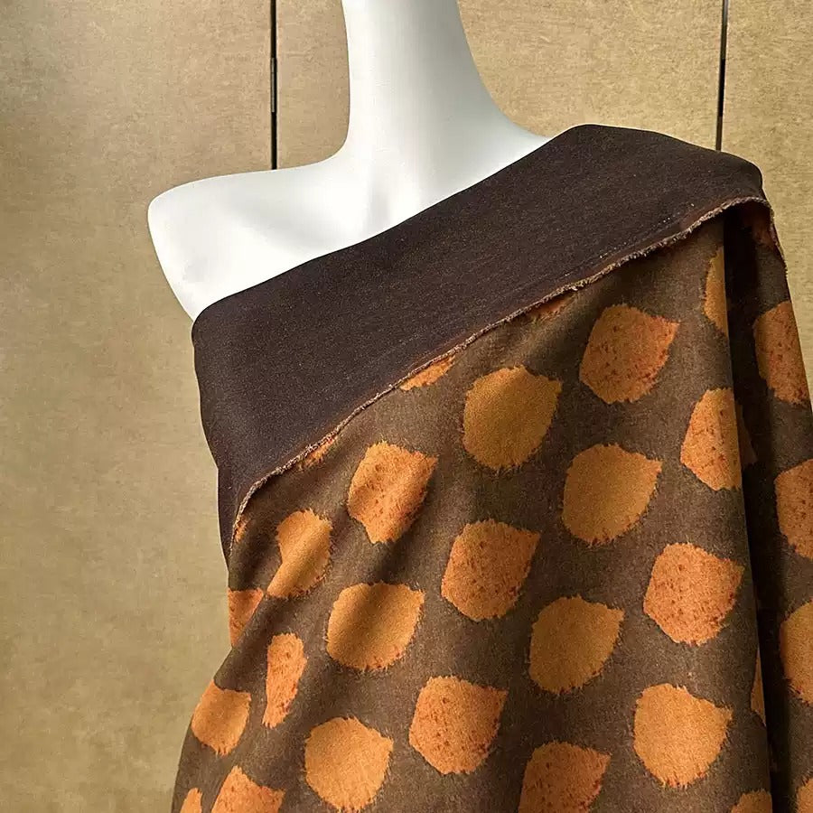 A mannequin wearing a brown and orange patterned fabric draped over its shoulder.