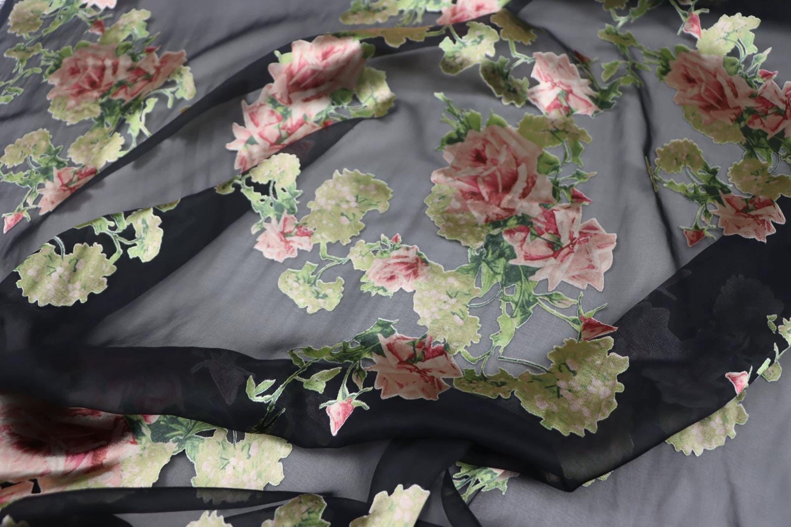 a close-up view of a fabric with a floral pattern, featuring pink and green flowers against a dark background.