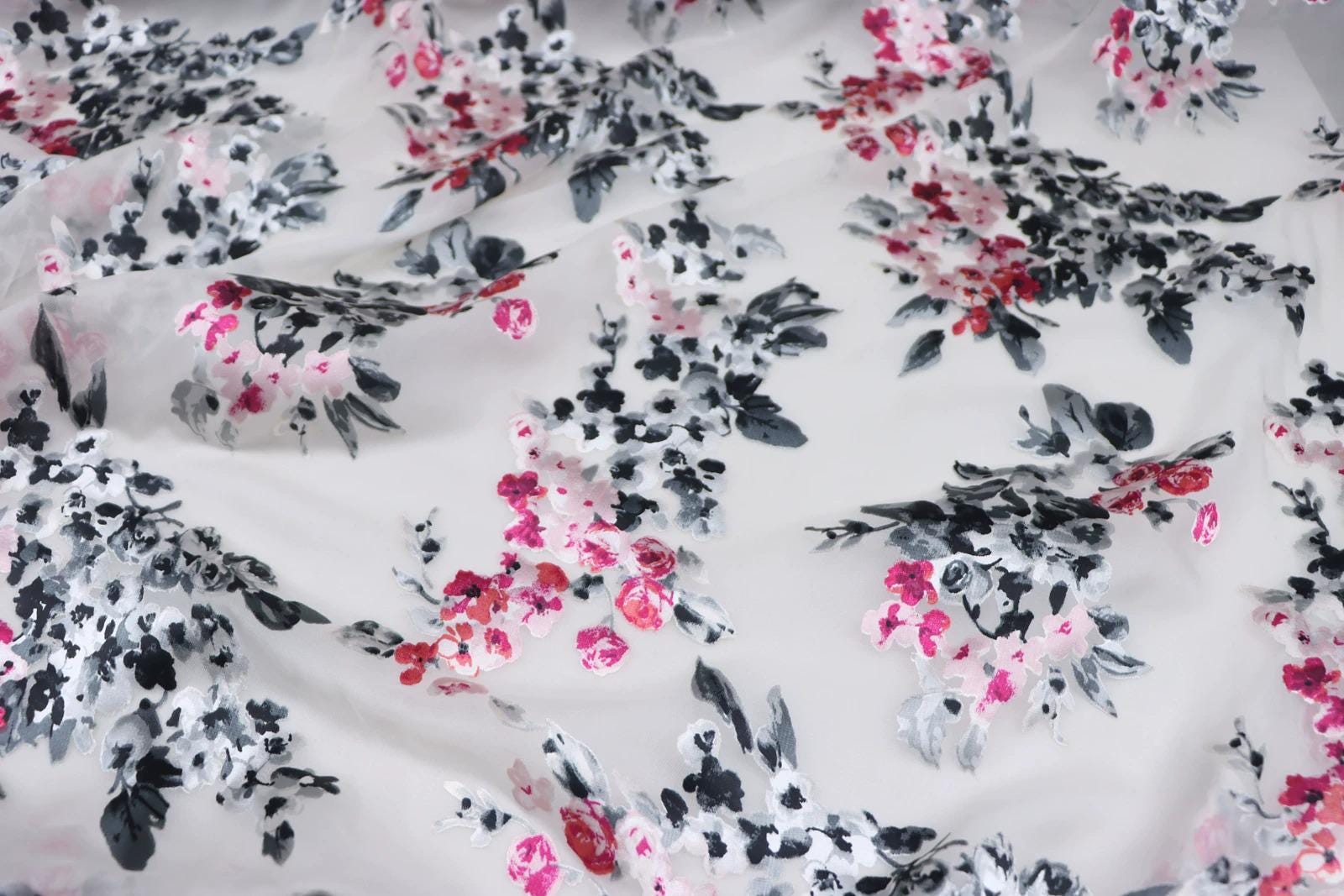 a close-up view of a fabric with a floral pattern in shades of pink and black. The pattern consists of various flowers and leaves, creating a visually appealing and intricate design.
