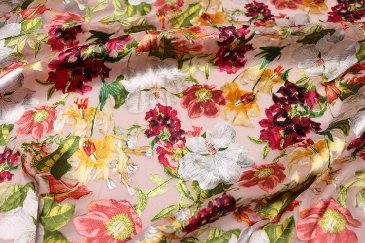 The image is a close-up of a fabric with a vibrant floral pattern, featuring a variety of colorful flowers and leaves.