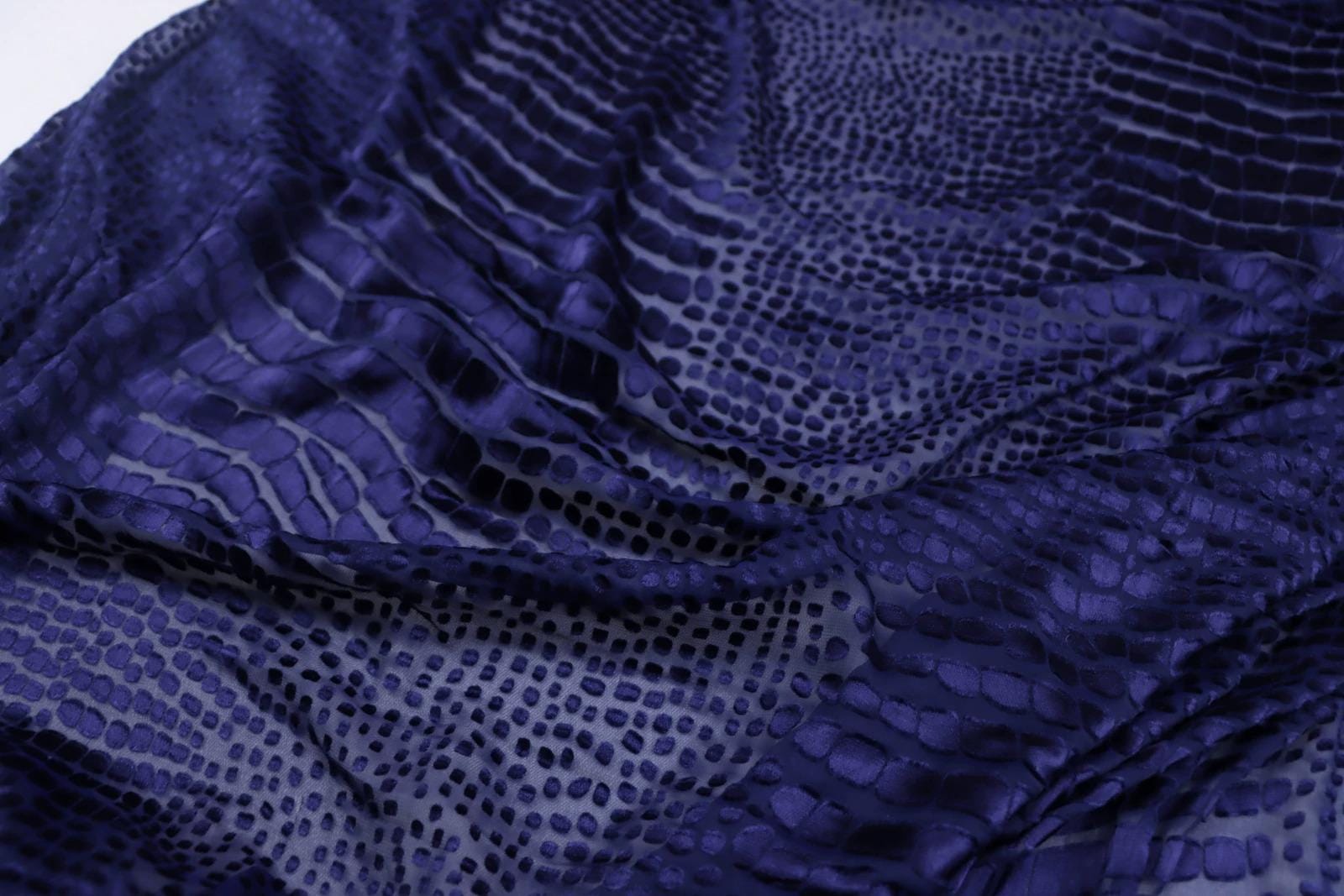 a close-up view of a fabric with a distinctive pattern of dark blue and gray dots or lines, resembling the scales of a snake or a crocodile.