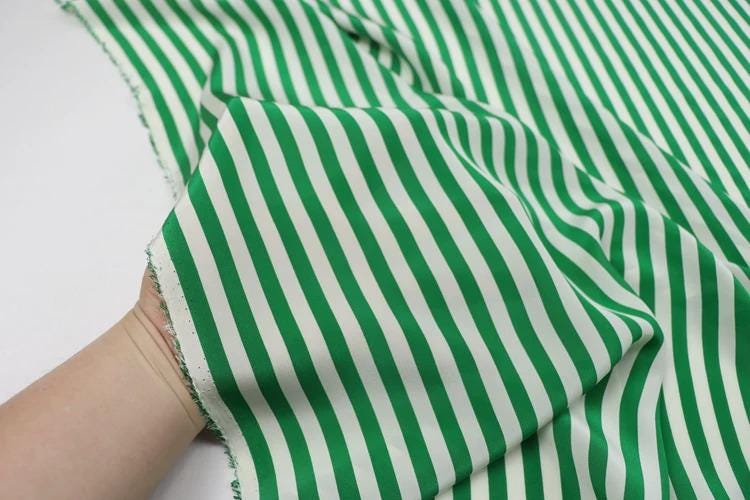A hand is holding a piece of fabric with green and white striped patterns.