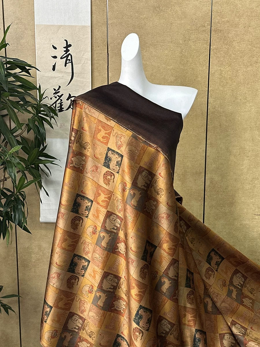 A mannequin wearing a brown and gold patterned fabric with various animal and human figures printed on it, displayed against a beige wall with a Chinese character hanging on it.