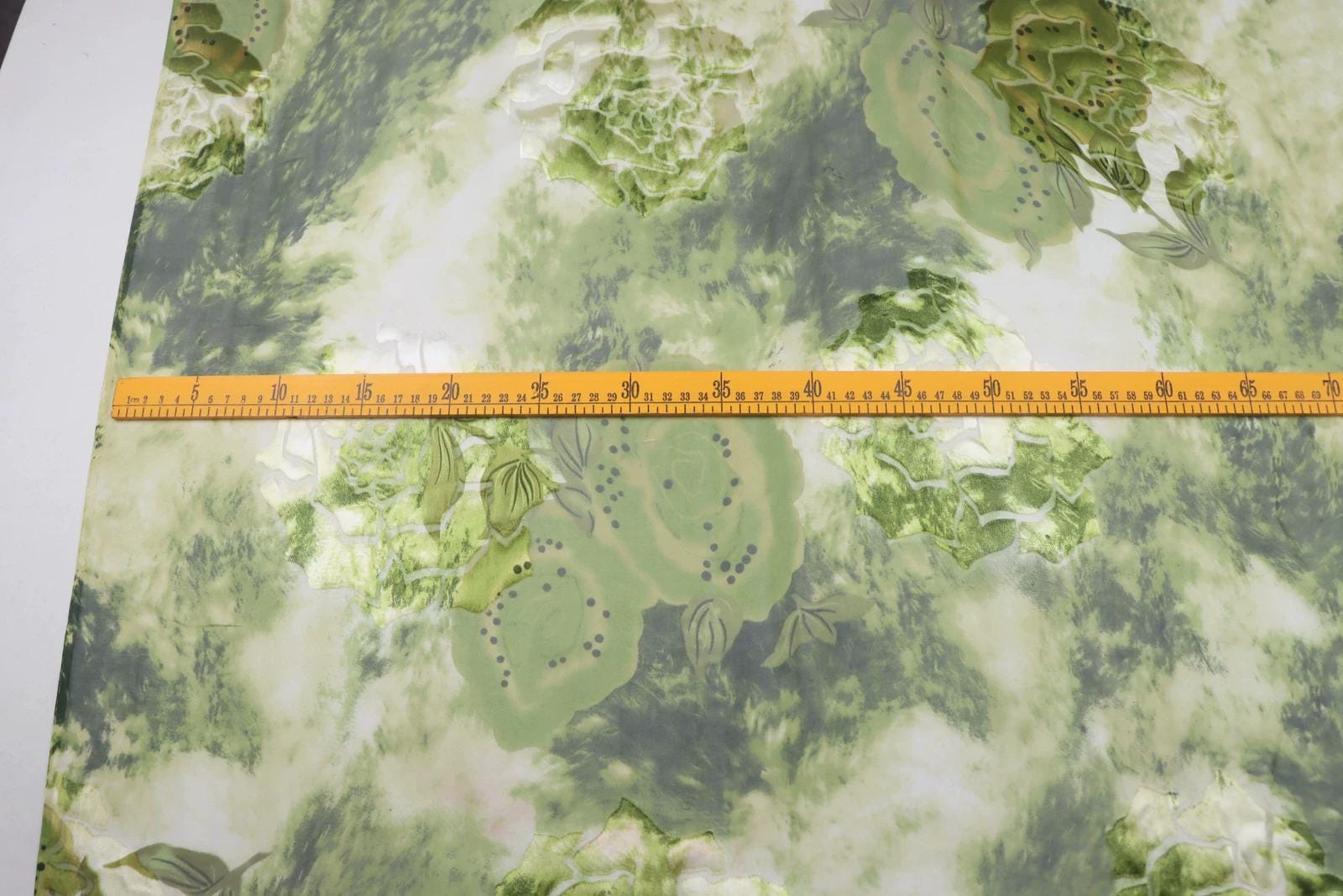 a fabric with a green and white floral pattern, and a yellow measuring tape is placed across it, indicating the size of the fabric.