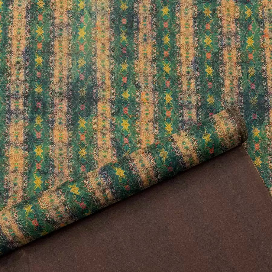 a close-up view of a colorful, patterned fabric with a repeating design of green and yellow stripes and small flowers or leaves. The fabric appears to be rolled up and placed on a brown surface.
