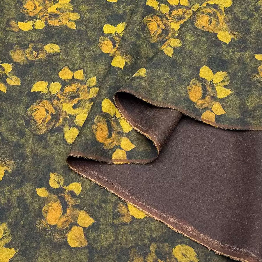 a close-up view of a fabric with a floral pattern in shades of green and brown. The fabric appears to be made of a dark-colored material, possibly a type of cotton or linen. The pattern consists of yellow flowers or leaves against a dark background, creating a visually striking contrast.
