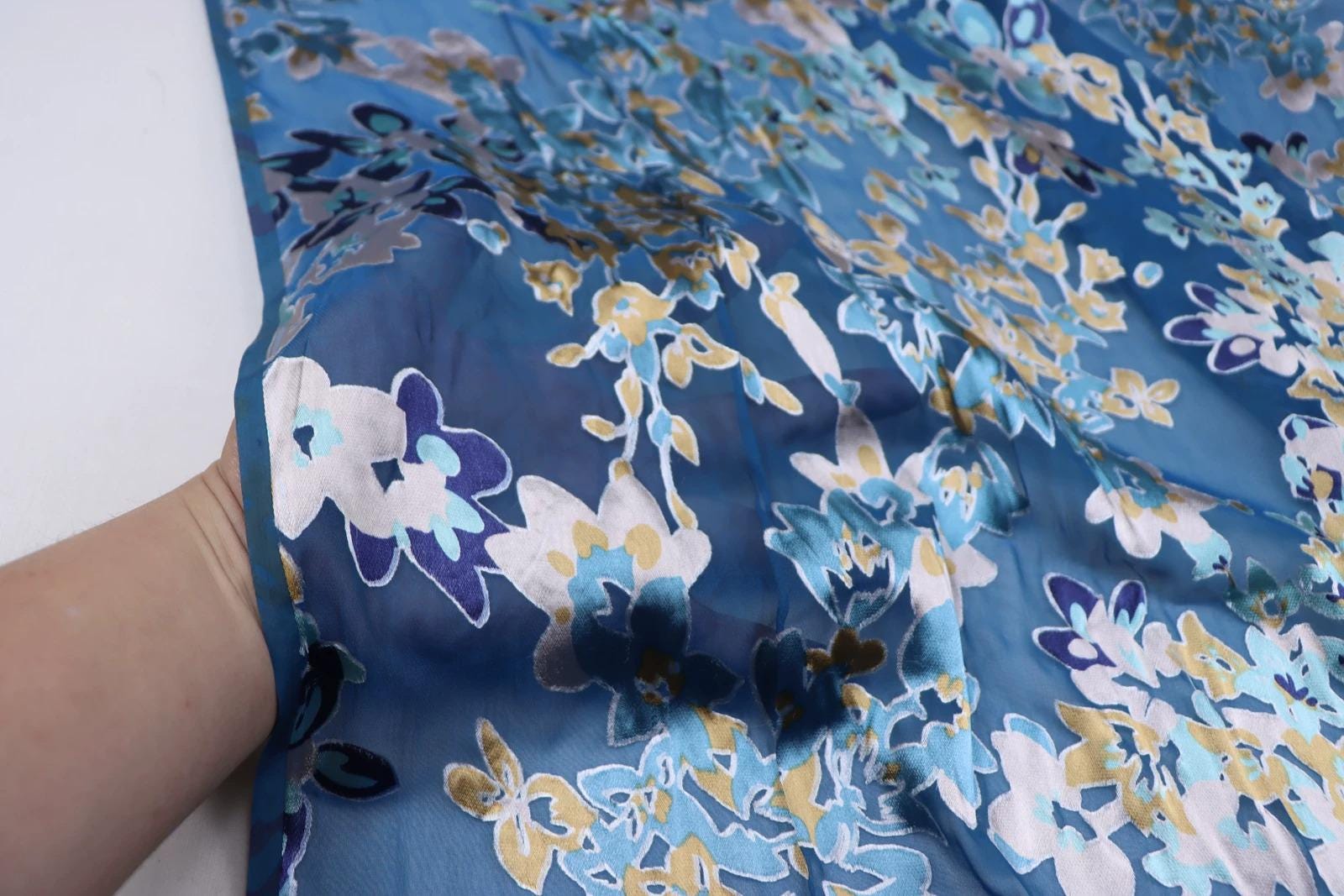 A close-up view of a blue fabric with a floral pattern, featuring various shades of blue, yellow, and white flowers.