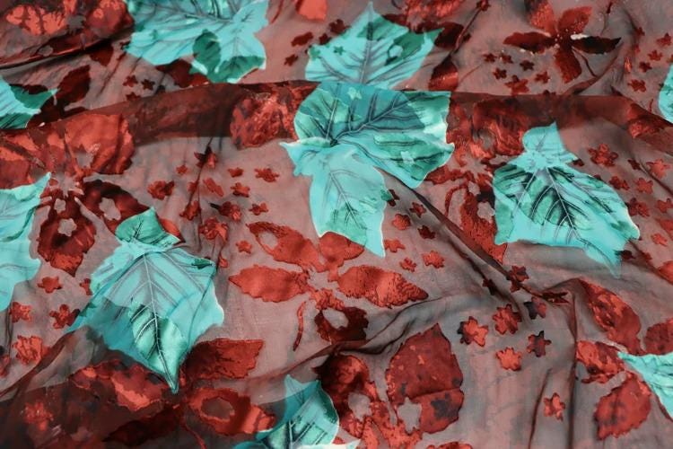 a close-up view of a fabric with a vibrant floral pattern. The fabric is adorned with a mix of red and green leaves, interspersed with small red flowers. The pattern is intricate and detailed, showcasing the craftsmanship of the fabric.