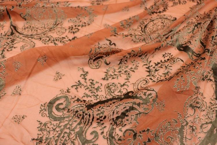 a close-up view of a fabric with a floral pattern in shades of orange and black. The fabric appears to be made of sheer material, with a delicate and intricate design.