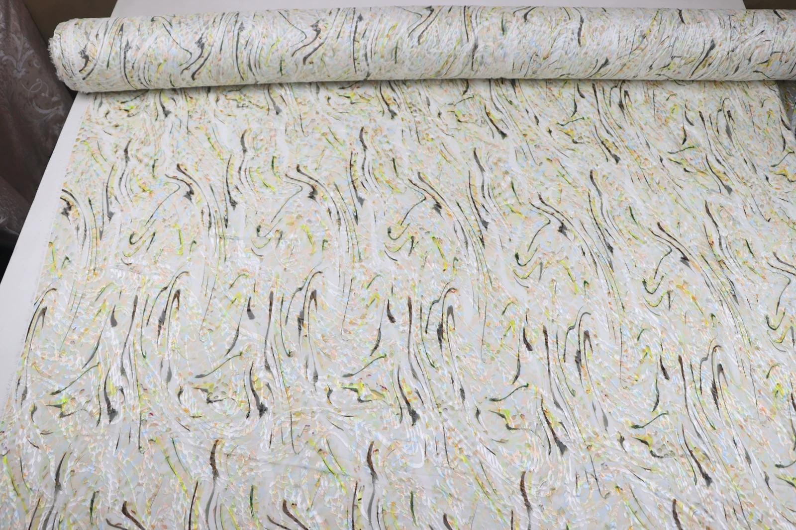 a roll of fabric with a repeating pattern of swirls and lines in various shades of white, yellow, and brown.