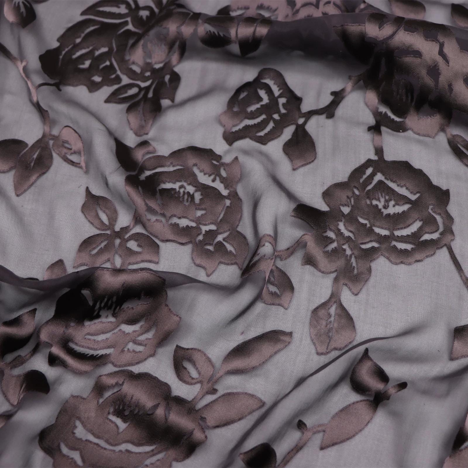 a close-up view of a fabric with a floral pattern, featuring dark brown or black rose-like designs.