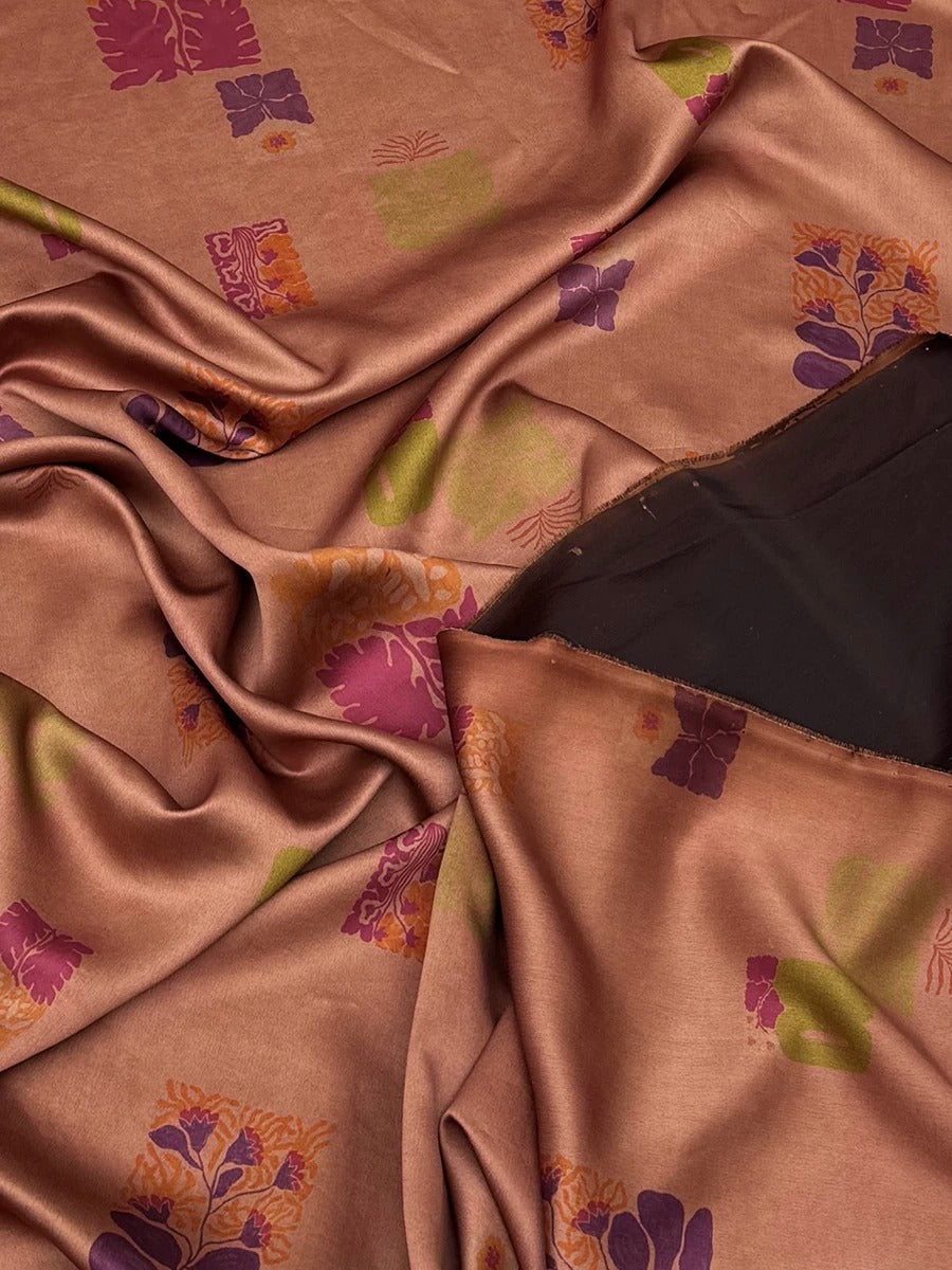 a close-up view of a fabric with a floral pattern in shades of pink and orange. The fabric appears to be made of silk or a similar material, and it is crumpled, giving it a soft and flowing appearance. The pattern consists of various flowers and leaves in different sizes and colors, creating a visually appealing and intricate design.