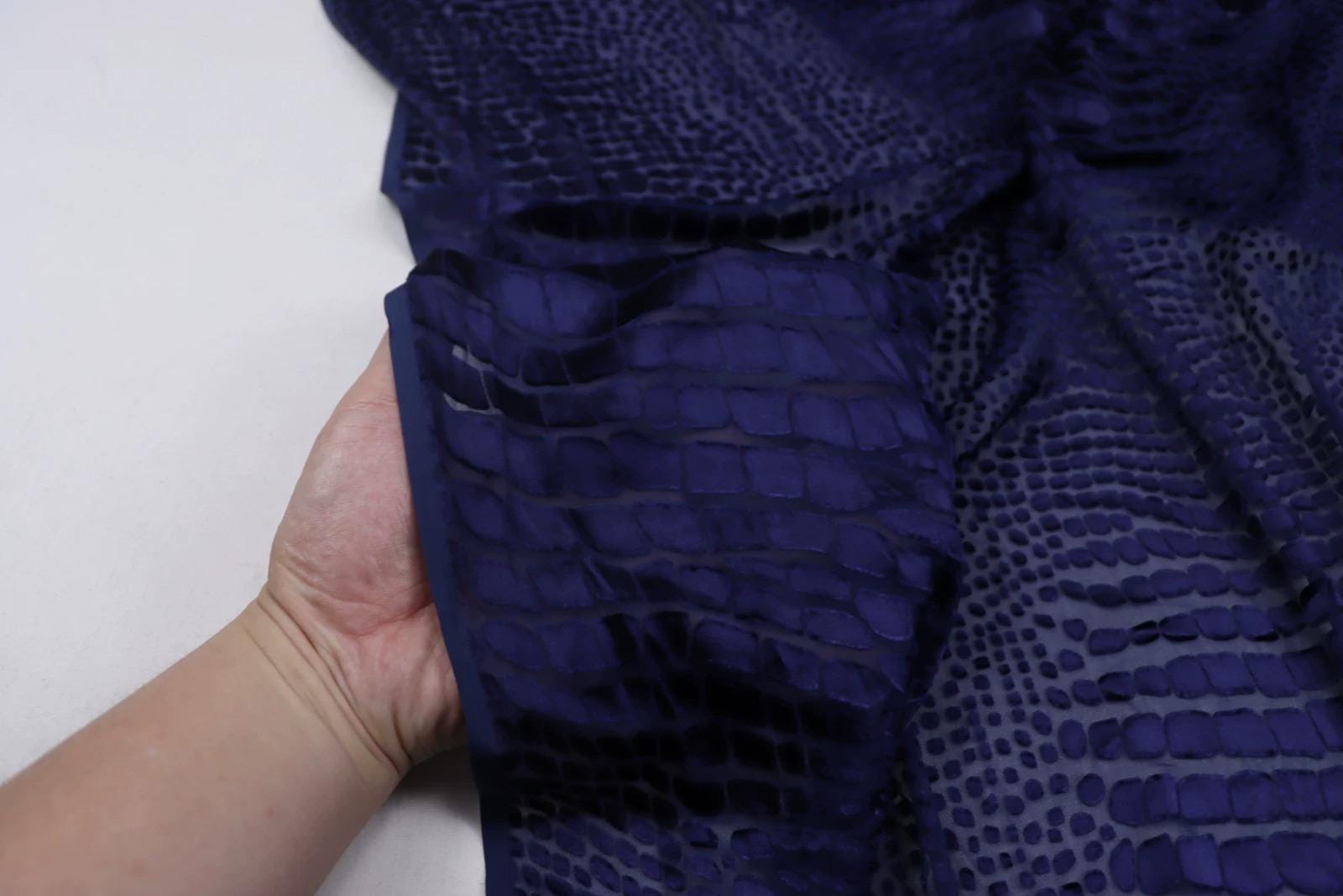 A hand is holding a piece of fabric with a pattern of small squares or dots in a dark blue color.
