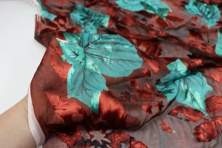 a close-up view of a fabric with a floral pattern in shades of red and green. The fabric appears to be made of silk or a similar material, and it has a textured appearance.