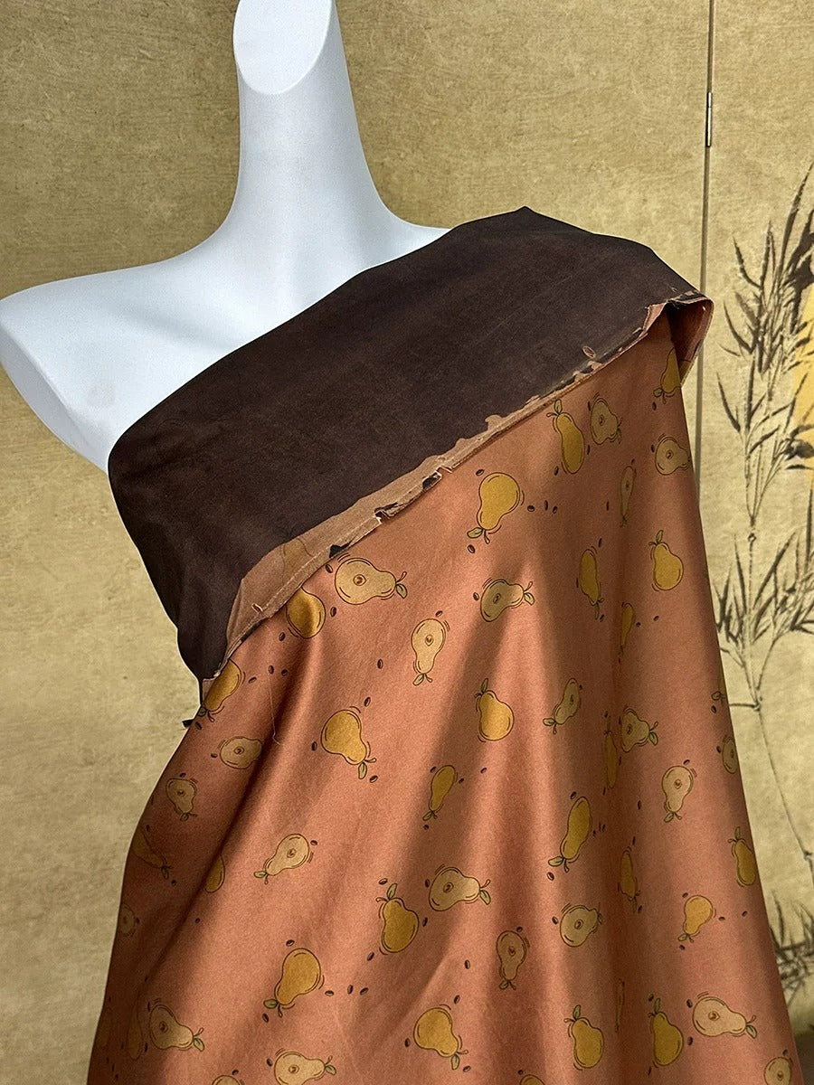 A mannequin wearing a brown and orange patterned fabric with a repeating pattern of small pear shapes.