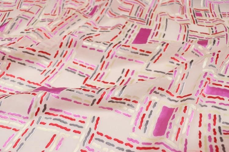a close-up view of a fabric with a geometric pattern of intersecting lines and shapes in various shades of pink, red, and gray.