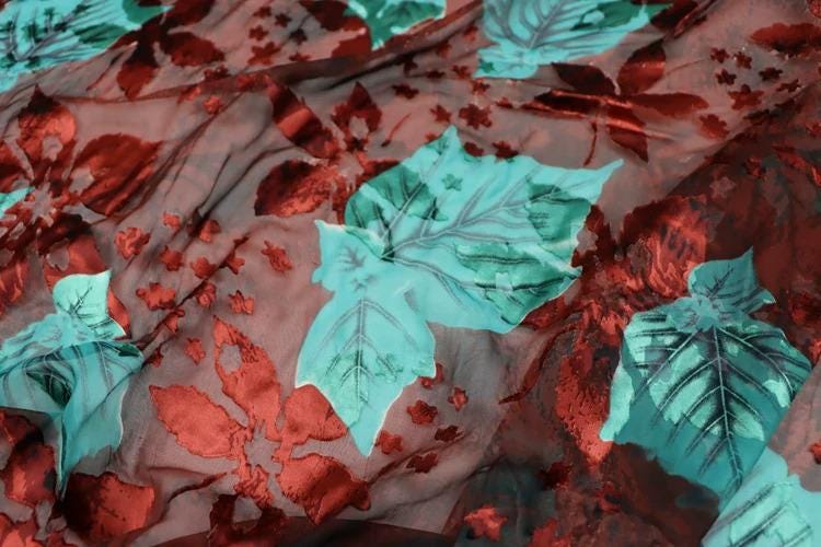 a close-up view of a fabric with a floral pattern. The fabric has a red background with green leaves and red flowers, creating a vibrant and colorful design.