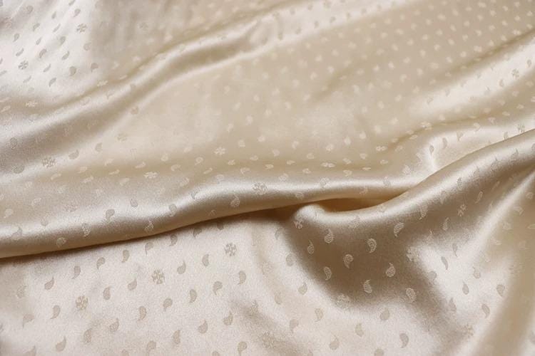 a close-up view of a fabric with a repeating pattern of small white dots or circles, creating a textured and shiny appearance.