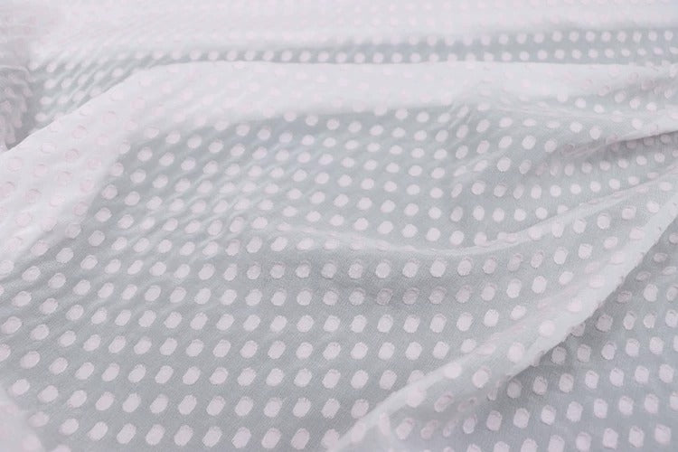 A close-up view of a fabric with a repeating pattern of small white dots or circles, creating a textured and visually interesting surface.