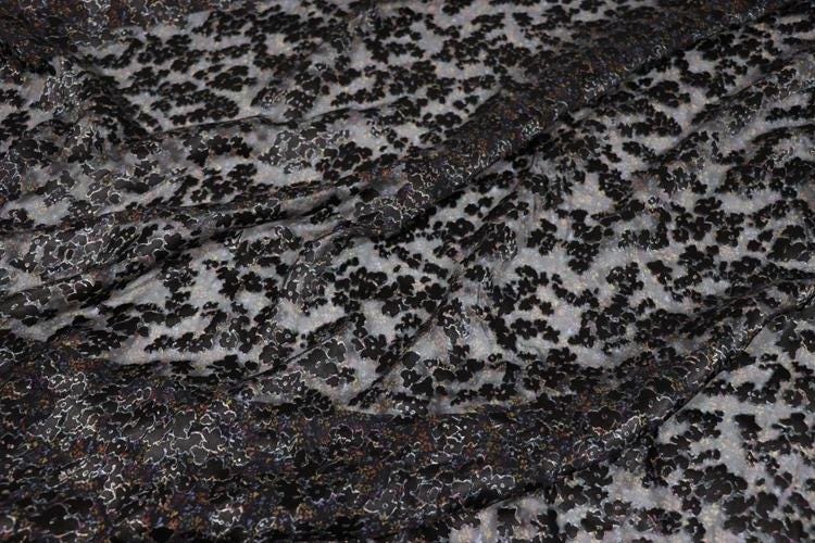 a close-up view of a fabric with a black and white floral pattern. The fabric appears to be made of a sheer material, with a black and white color scheme. The pattern consists of small black flowers or leaves scattered across the fabric, creating a visually striking contrast against the lighter background.