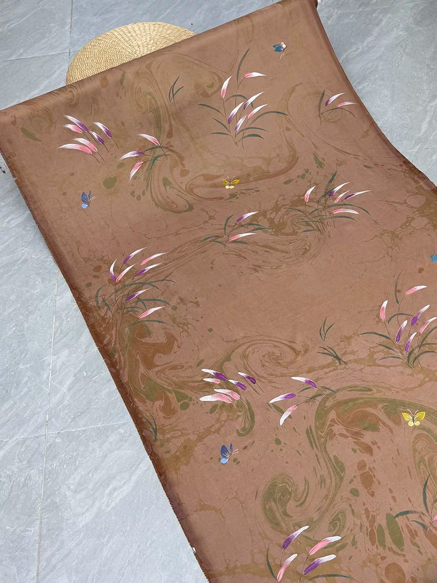 a brown fabric with a floral pattern, including pink and green flowers, butterflies, and leaves. The fabric appears to be a piece of clothing or textile with a decorative design.