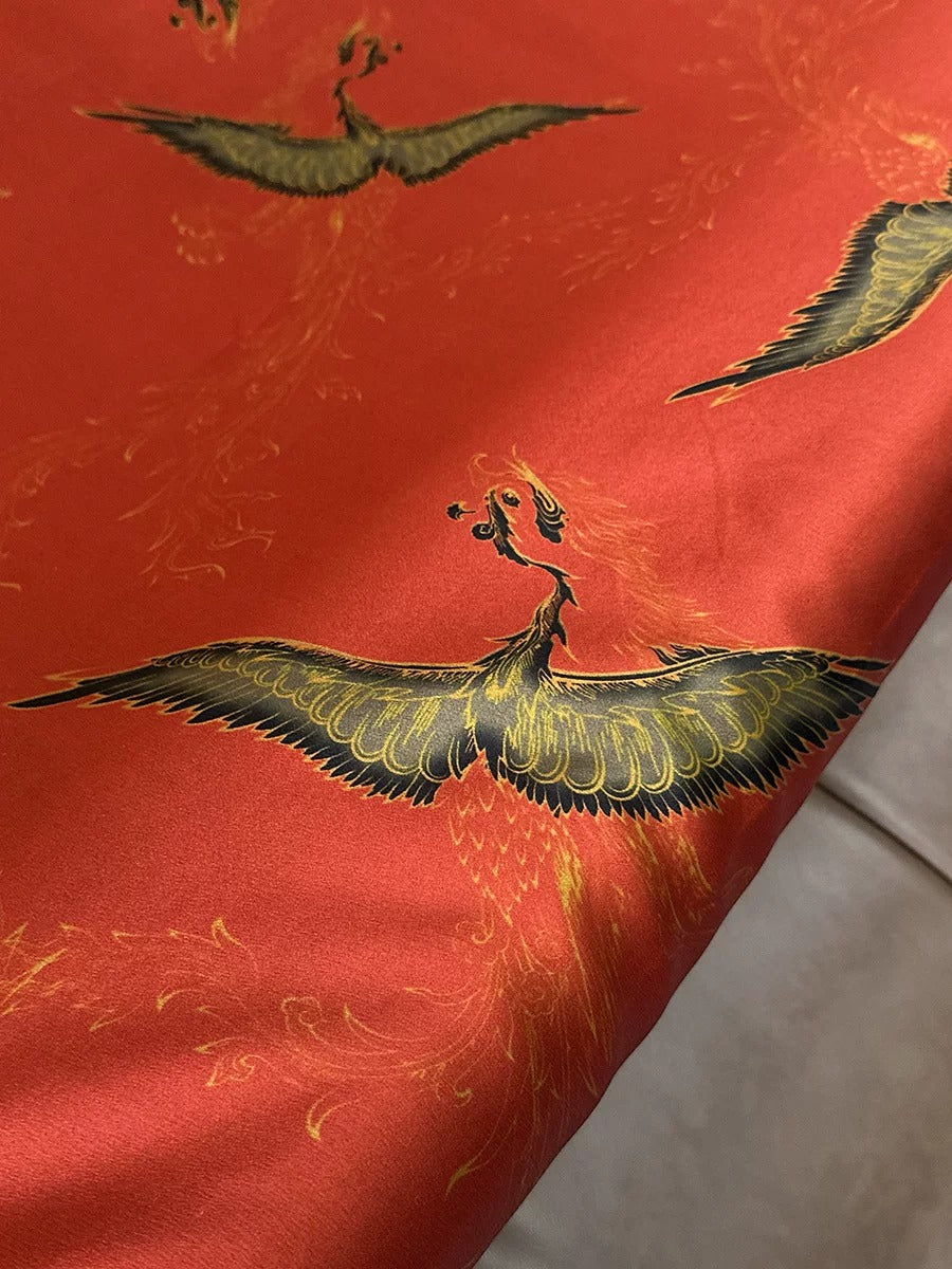 a close-up view of a vibrant red fabric with a striking black and gold design of stylized birds, including a phoenix, on it.