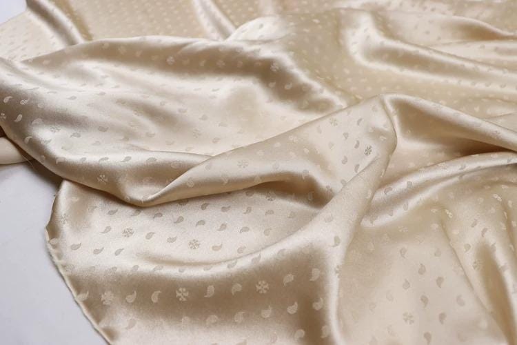 a close-up view of a crumpled, beige satin fabric with a repeating pattern of small white dots or circles.