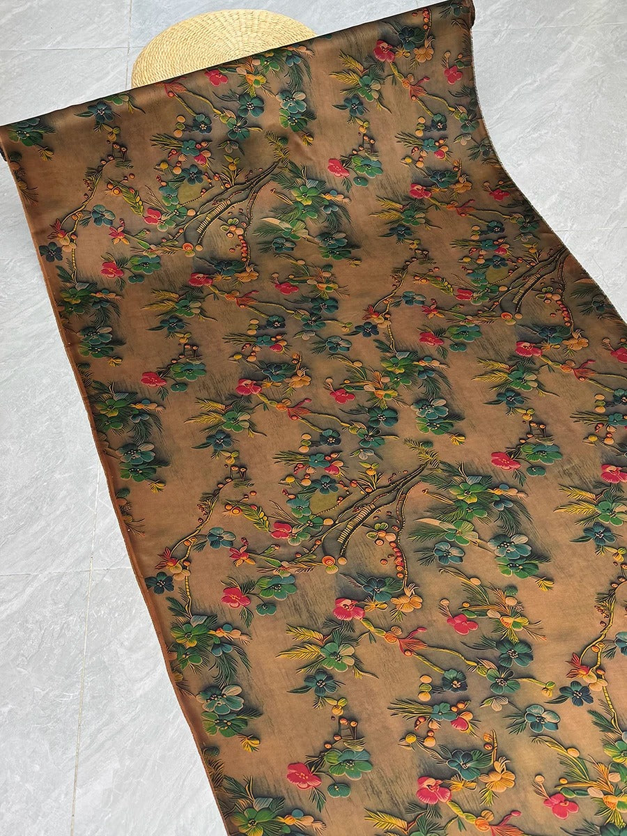 a brown fabric with a floral pattern, including various shades of green, red, and yellow flowers and leaves. The fabric appears to be rolled up and placed on a white surface.
