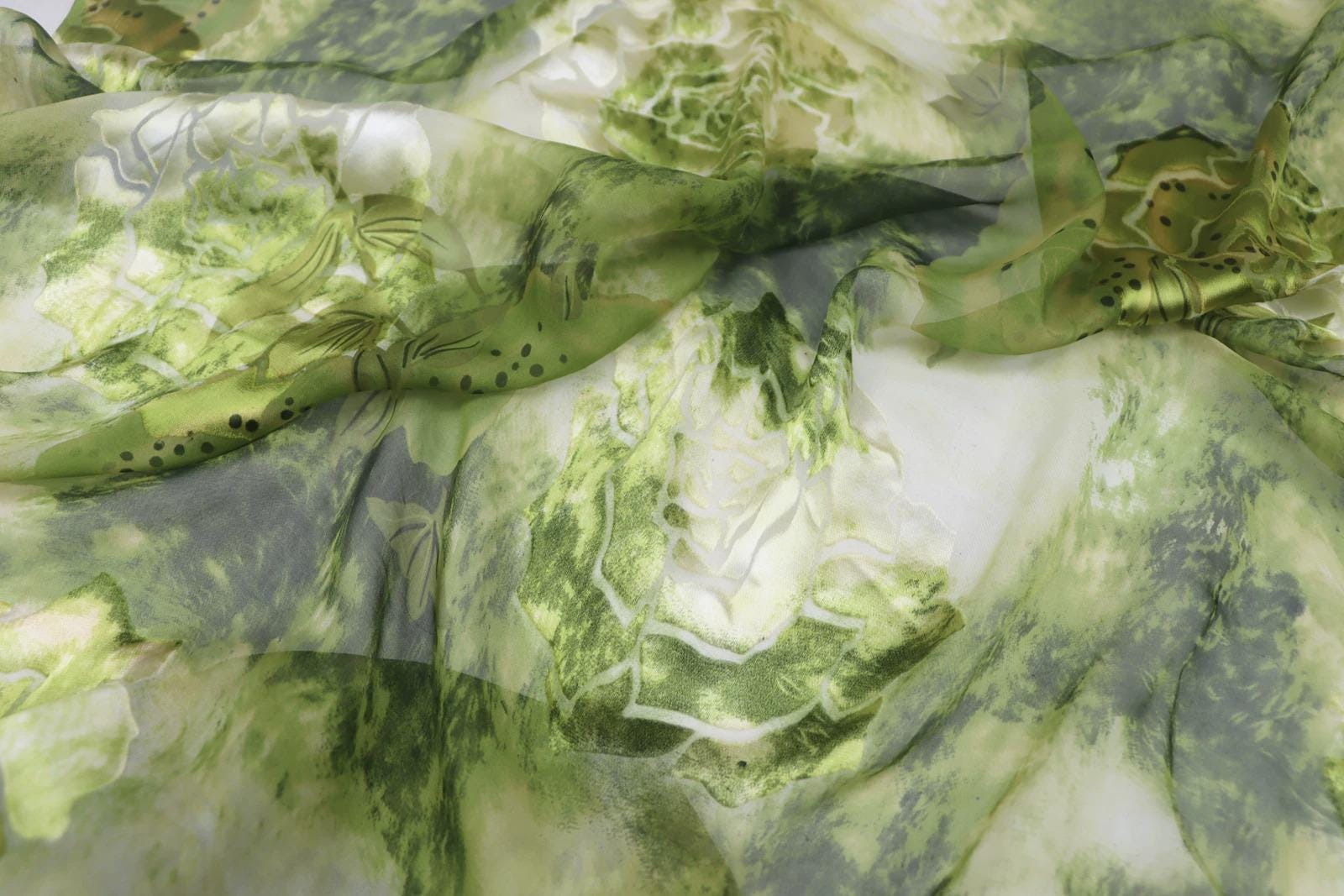 The image is a close-up of a fabric with a green and white floral pattern. The fabric appears to be made of silk or a similar material, and it has a slightly wrinkled texture. The pattern consists of various shades of green and white, creating a visually appealing and intricate design.