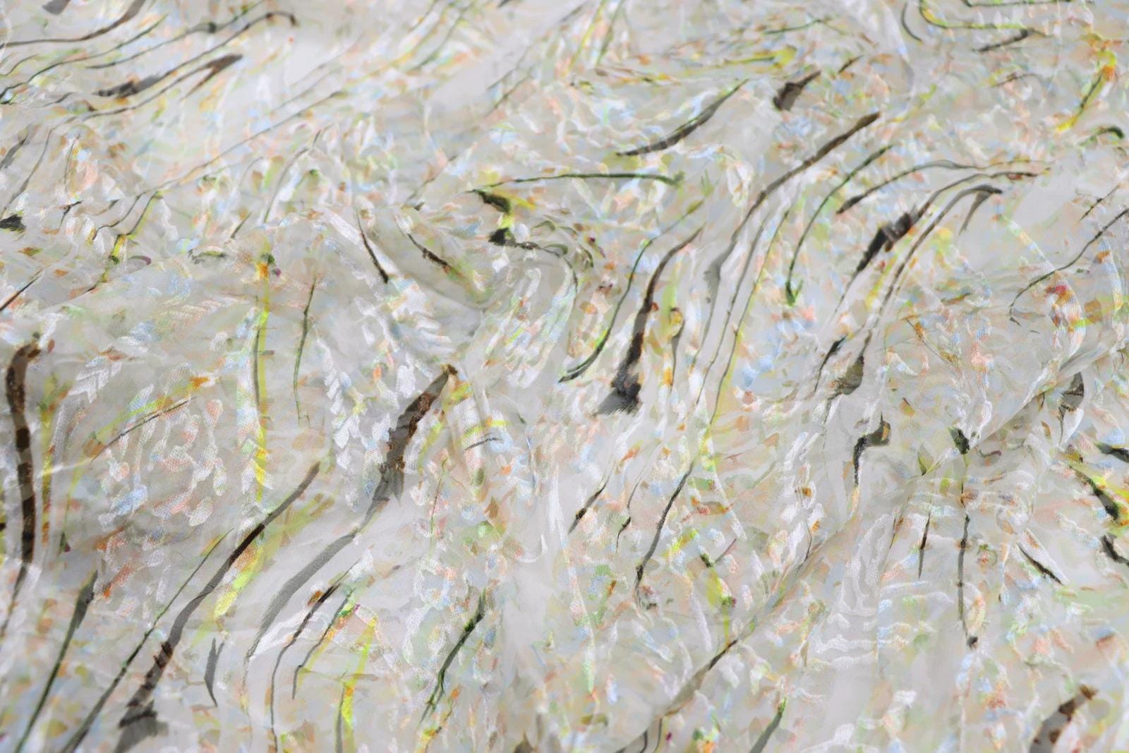The image is a close-up of a textured fabric with a pattern of thin, wavy lines in various shades of white, yellow, and green. The lines appear to be made of a translucent material, giving the fabric a soft, flowing appearance.