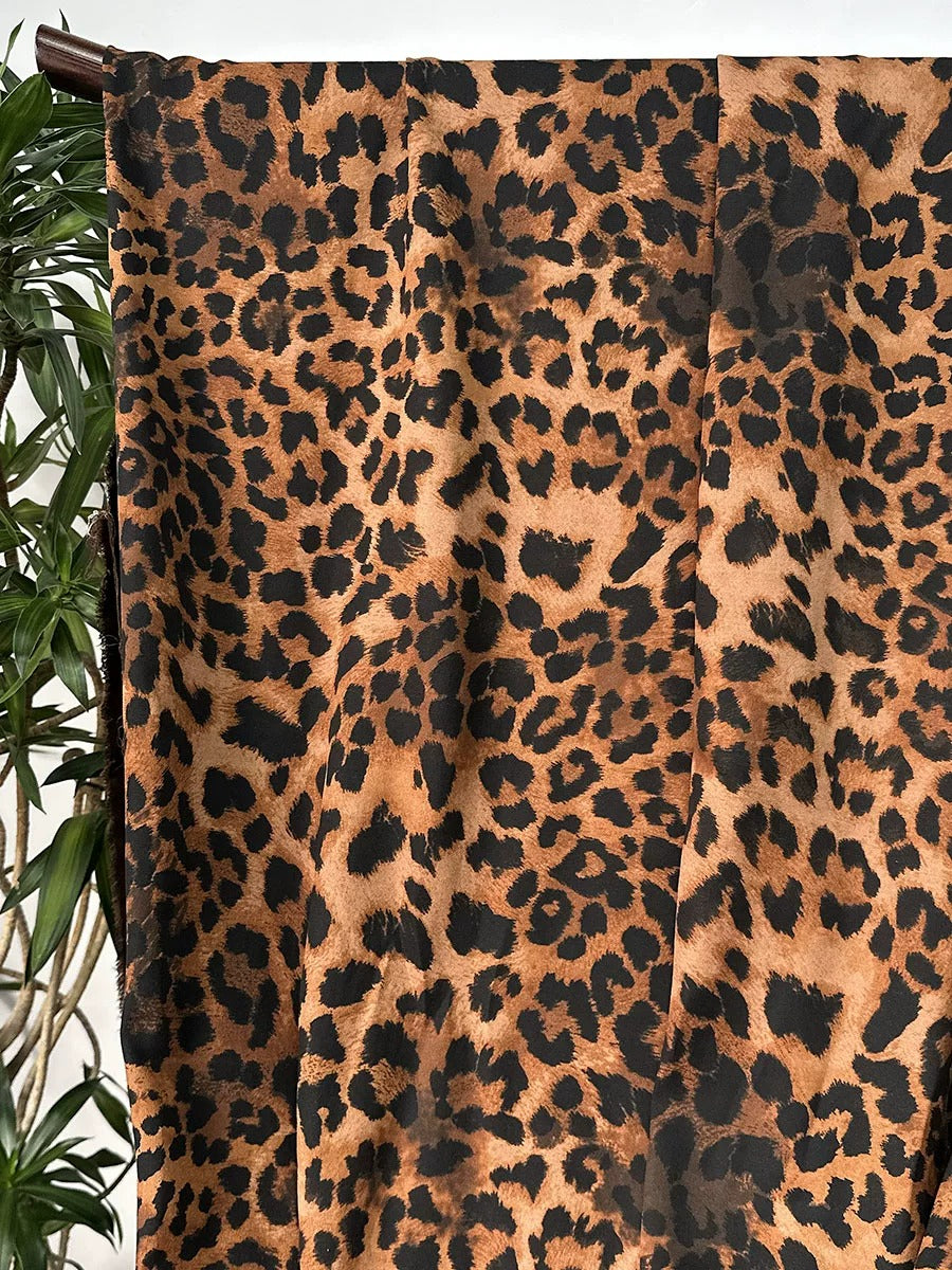 a leopard print fabric hanging on a wall, with a plant visible to the left side.