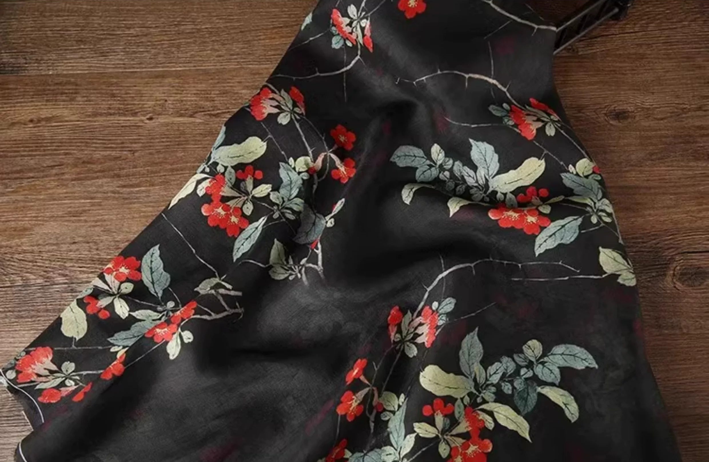 a black fabric with a floral pattern of red flowers and green leaves.