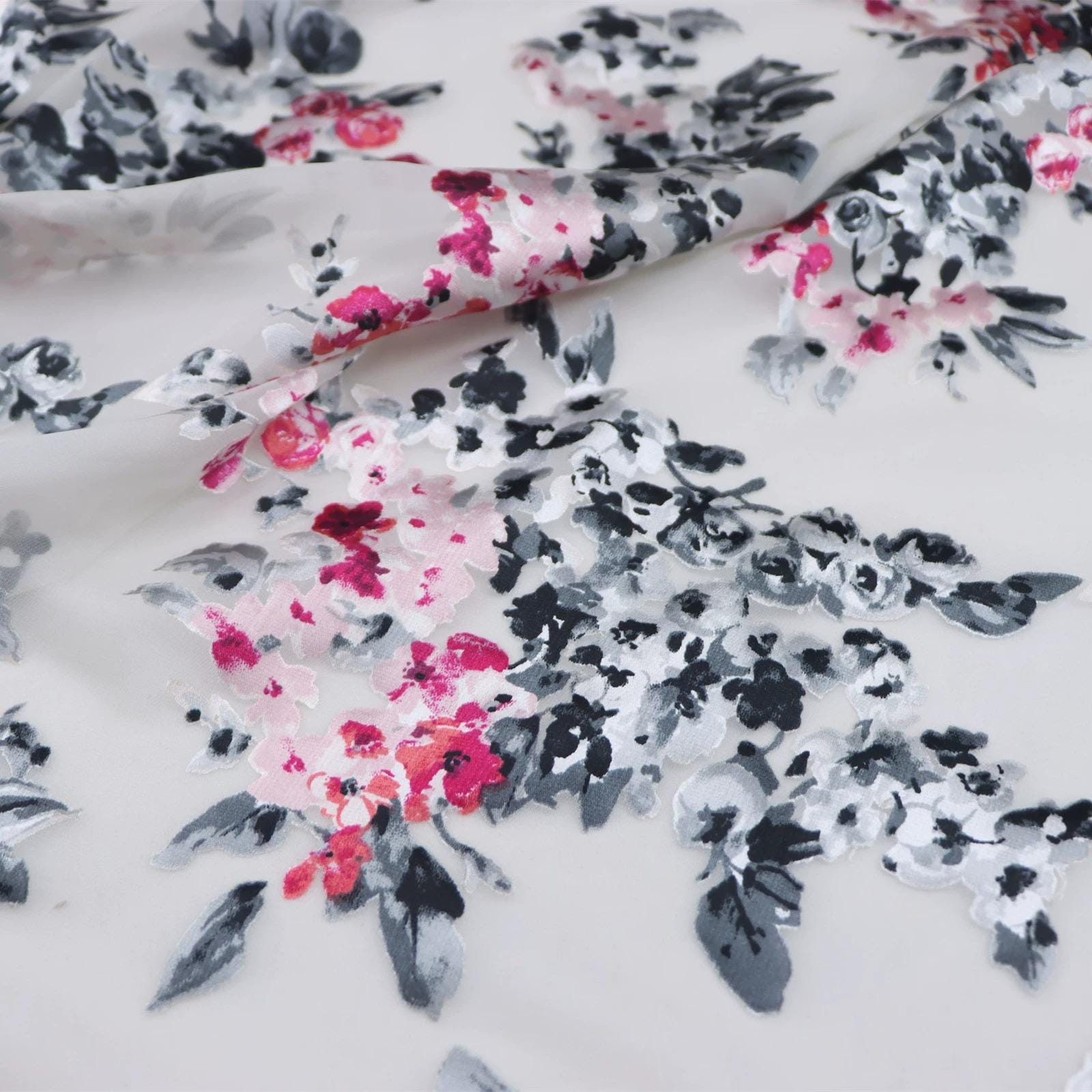 a close-up view of a fabric with a floral pattern. The fabric appears to be white and has a black and pink floral design. The pattern consists of various shades of pink and black flowers, along with some white flowers, creating a visually appealing and intricate design.