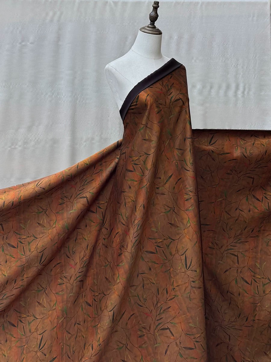 A mannequin wearing a large, flowing dress with a pattern of leaves and branches on it.