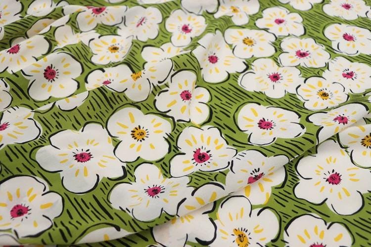 a close-up view of a fabric with a repeating pattern of white flowers with yellow centers against a green background.
