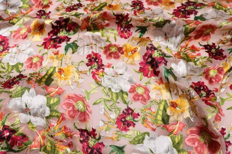 a close-up view of a fabric with a vibrant floral pattern. The fabric is covered in a variety of colorful flowers, including red, white, yellow, and green, creating a visually striking and lively design. The pattern appears to be a repeating motif, with the flowers arranged in a way that fills the entire fabric surface.