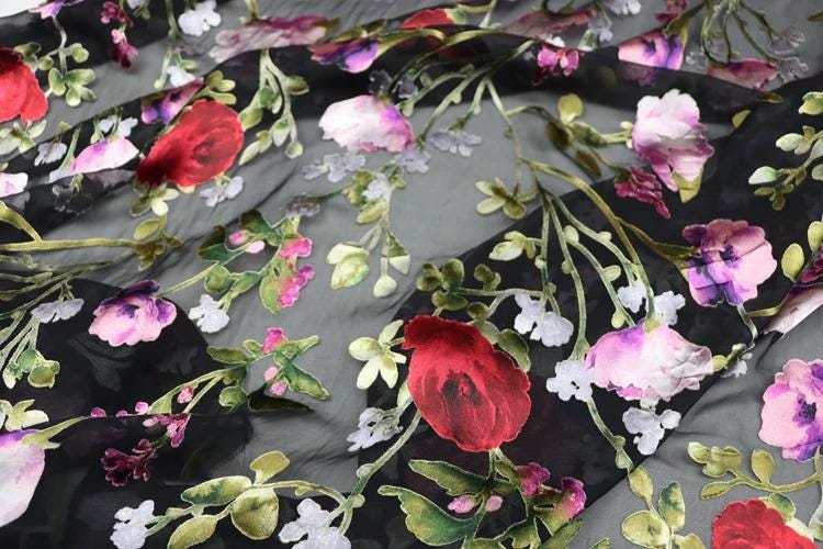 a close-up view of a fabric with a floral pattern. The fabric is predominantly black, with red and white flowers and leaves scattered across it. The flowers appear to be the main focus of the image, with the leaves providing a contrasting background. The overall composition of the image is visually appealing and showcases the intricate details of the floral pattern.