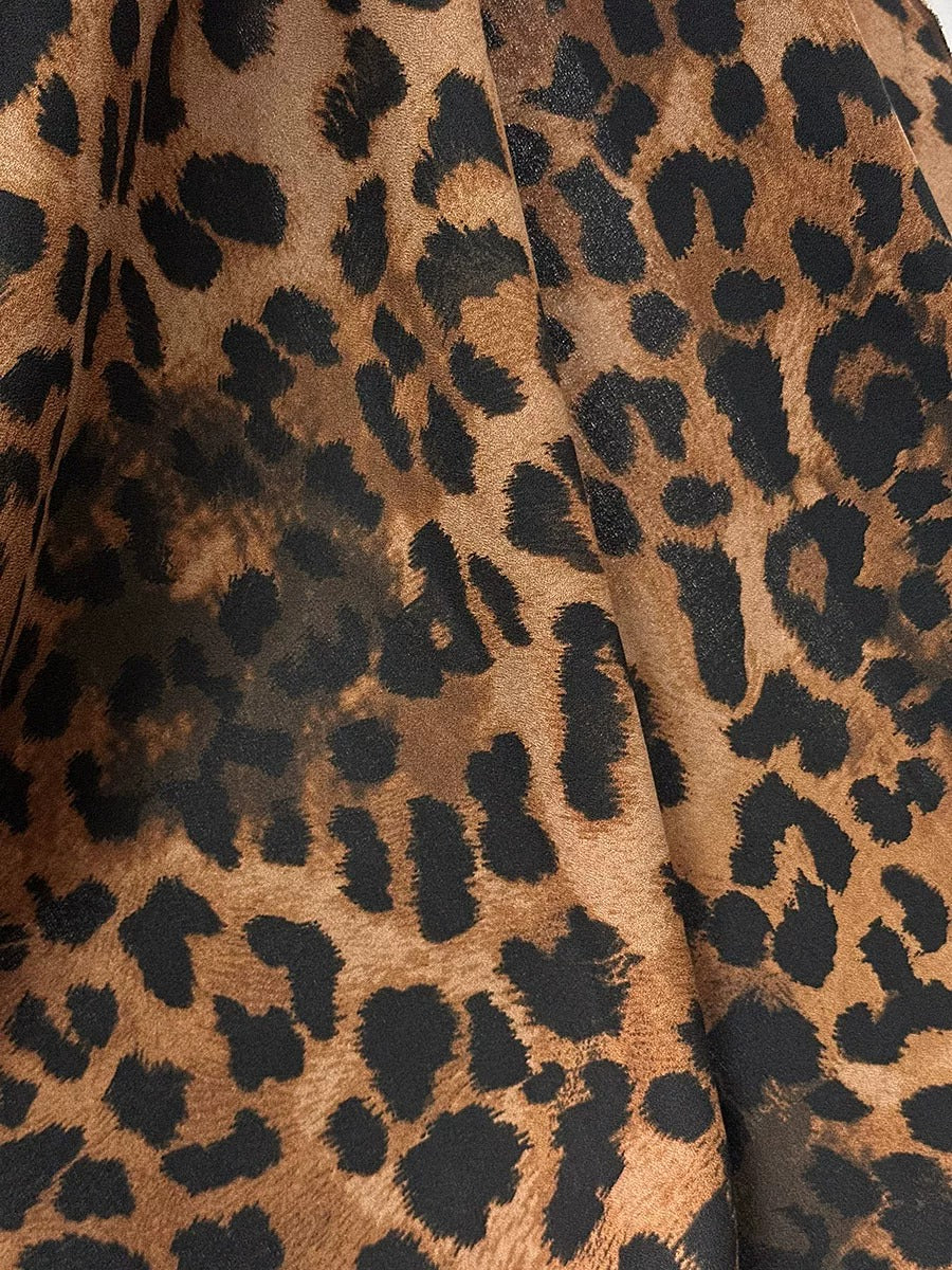 a close-up view of a fabric with a distinctive leopard print pattern. The fabric appears to be a dark brown color, with a mix of black and brown spots that resemble the distinctive markings of a leopard. The pattern is intricate and detailed, creating a visually striking and eye-catching design.