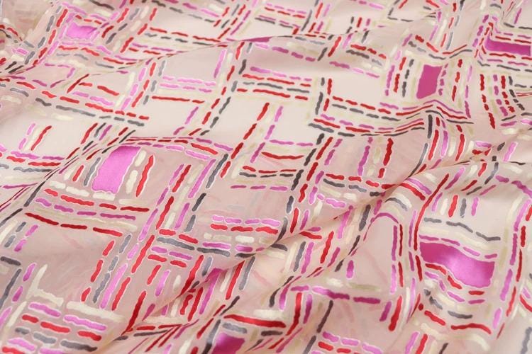 a close-up view of a fabric with a repeating pattern of pink, red, and gray stripes or lines. The pattern is intricate and detailed, creating a visually striking and textured appearance.