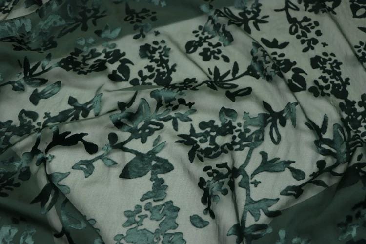 a close-up view of a fabric with a floral pattern, featuring various shades of green and black.