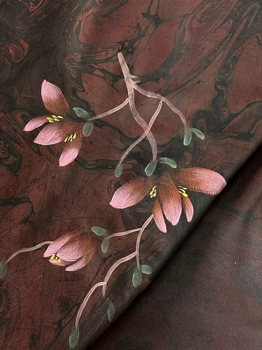 a close-up view of a dark red fabric with a floral pattern. The fabric has a marbled texture, and there are pink flowers with green leaves on it.